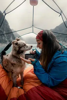 Dentro de una tienda de campaña un perro y su amo disfrutan de la anturaleza y del momento.