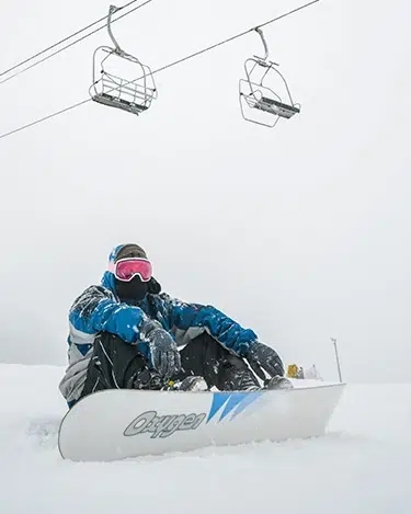 persona sentada en la nieve mostrando su material de snowboard