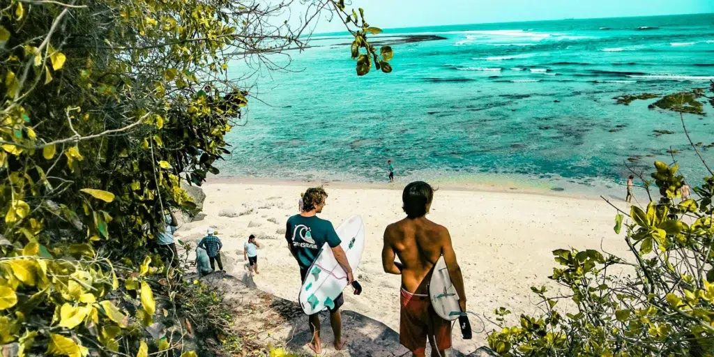 dos personas llegando con tablas de surf a una playa